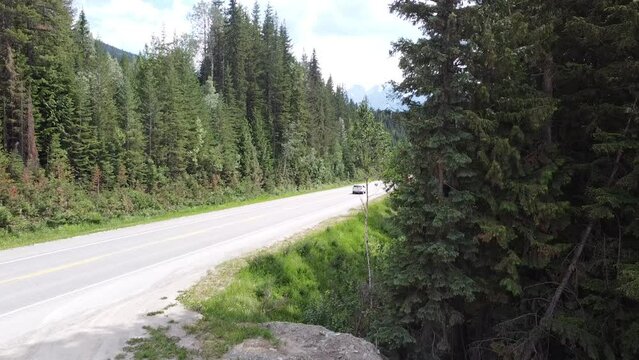 Cars Driving on Highway Road - Still Video - Rocky Mountains BC Canada. Cars passing by on a scenic road with trees and mountains surrounding them.