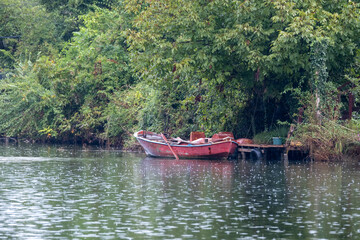 A red boat on the river in the forest. The reflection of the boat on the water. Colors of nature, rainy day.