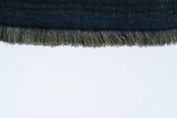 A strip of dark blue jeans with thread fringe on top of a white sheet