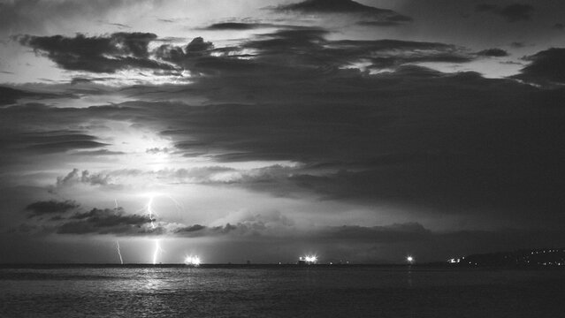 Epic photo of the sky over the sea with lightning in the clouds. Spectacular nature show. Long exposure photography, night landscape in black and white.