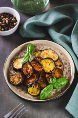 Pieces of fried eggplant with spices and basil on a plate on the table vertical view