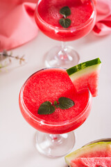 Watermelon lemonade with watermelon pieces in glasses on pink background vertical view