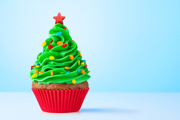Cupcake. Christmas Tree cupcake with star on top. Red cup liners. Merry Christmas. Tasty baking cupcakes, cake or muffin with green cream icing, frosting and colored sprinkles. Bakery, confectionery. 