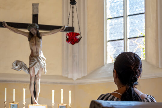 Woman sitting in a lighted Catholic church, looking at the altar, back view.