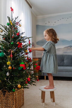Cute little child girl is decorating the Christmas tree indoors. Merry Christmas and Happy Holidays! Christmas eve. Holiday Activity for Kids.