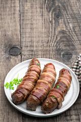 Appetizing sausages wrapped in bacon and grilled on white plate on wooden table