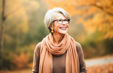 Portrait in the forest of a pleased 70 years old woman. Joyful woman in an  outdoor fall scenery having fun at the autumn season. 