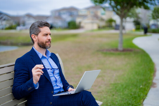 Business man in suit sitting on bench. Business man on bench in park outdoors. Thinking about business. Thoughtful businessman, freelancer work on laptop on american neighborhood. Free business.