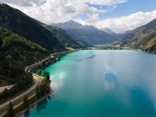 Aerial drone view of Poschiavo alpine lake and road in the Switzerland mountains. Miralago Bernina Express train station. Swiss Alps	
