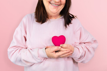A mature woman smiles while holding a pink resin heart, symbolizing hope and support for breast cancer awareness, ideal for October Pink campaigns