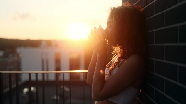 Portrait of stunning young woman take sip drinking hot tea or coffee with beautiful sunset or sunrise at home balcony Calm relaxed female enjoying leisure time alone indoors