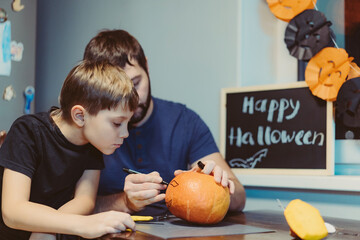 caucasian man with child carving a traditional Jack lantern from pumpkin. Halloween concept. Image with selective focus