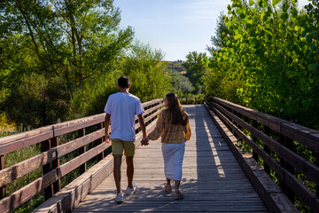 Fototapeta na wymiar boy and girl in love walking along a wooden bridge holding hands on a sunny day
