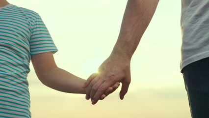 Adoption of child. Child son and dad hold hands close-up in nature in sun. Happy family, teamwork. Child father walk in spring park at sunset, family trust concept. Parent, kid boy outing together