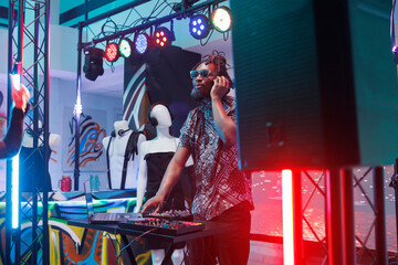 Dj in headphones mixing sounds using digital electronic music controller on stage in nightclub. Young african american man musician performing at discotheque party in club