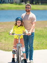 Happy Fathers day. Father and son in bike helmet for learning to ride bicycle at park. Father helping son cycling. Father and son on the bicycle on summer day. Kid son trying to ride bike with father.