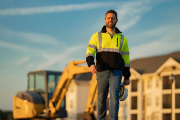 Construction man with excavator at industrial site. Worker in helmet build with bulldozer. Engineer work with builder contractor in hardhat. Excavation foreman with tractor. Workman with excavator.