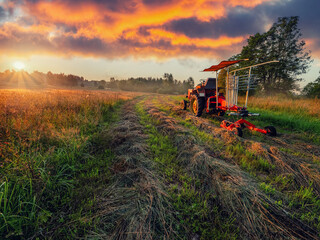 Fototapeta premium Old rusty tractor with grass cutting machine in a agriculture field with tall grass at stunning sunrise. Farming industry. Beautiful nature scene at special time. Nobody.