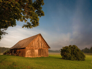 Obraz premium Old wooden barn in country side. Rural area in Latvia. Place for storage made of wood, simple construction local material. Living on a farm. Nobody. Beautiful nature scene.