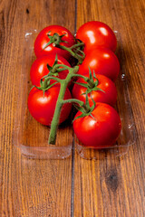 Fresh ripe tomato on a vine in plastic tray on wooden table surface. Organic product. Food supply chain industry. High quality vegetable.