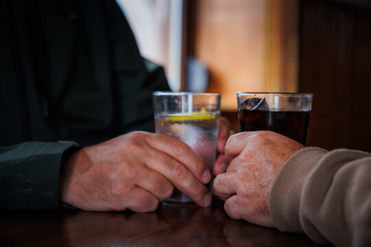 Two drinking glasses of two friends at the bar with their hands on a wooden table