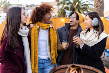 Diverse group of people having fun together at christmas market in winter. Multiracial young adult...