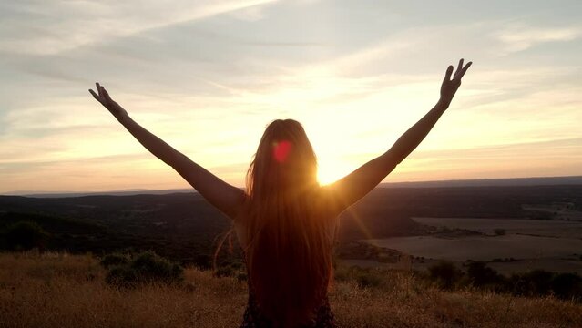 Unrecognizable female traveler opens her arms as a symbol of freedom during a sunset. Concept of travel, freedom
