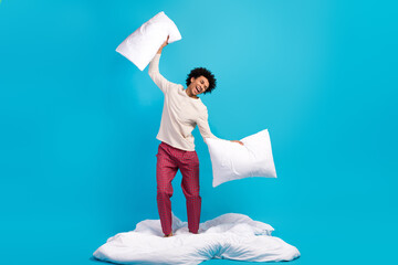 Full size photo of nice carefree young man stand white blanket hands hold pillows isolated on blue...
