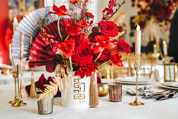 Floral arrangement, festive bouquet, table decoration for Chinese New Year party celebration in restaurant. Traditional red gold color decor. Roses,poppies,fan,candles,tassels. Chinese lunar calendar