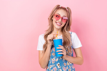 Photo of good mood dreamy woman dressed flower print overall in sunglass look empty space hold soda cup isolated on pink color background