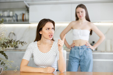 Two young upset women during quarrel in kitchen at home