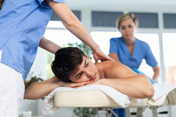 Relaxing professional massage for a young man in a spa salon is done by two women