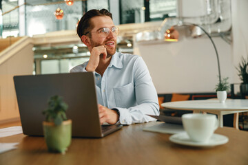 Smiling male manager drinking coffee during working on laptop in modern office . High quality photo
