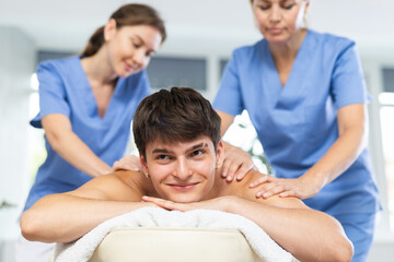 Two female masseurs massaging a man in a spa complex