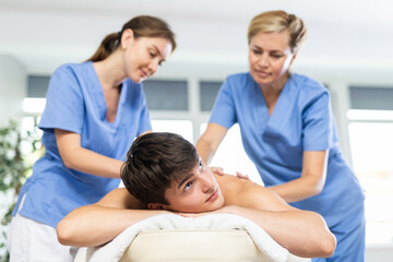 Fototapeta na wymiar Two women doing back massage to man lying on massage table in a spa salon