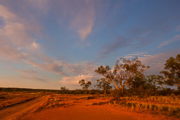 Obraz premium A dirt road in typical semi arid country at sunset with sky and clouds in Currawinya National Park in Australia