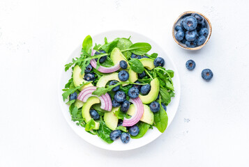 Gourmet vegan salad with blueberry, avocado, red onion, spinach, arugula and mixed herbs, white table background, top view