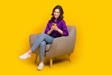 Full body portrait of gorgeous positive lady sit comfy chair use smart phone texting isolated on yellow color background