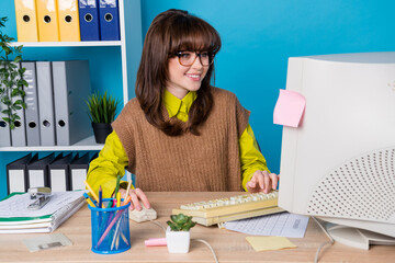 Photo of cheerful cute woman dressed knitted waistcoat eyewear working office typing obsolete device isolated blue color background