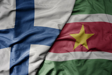 big waving national colorful flag of finland and national flag of suriname .