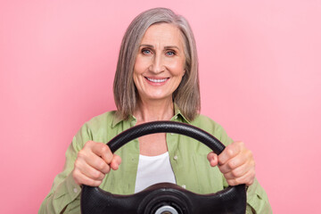 Photo of cheerful lovely senior lady pensioner wear green trendy clothes drive car first time city roads isolated on pink color background