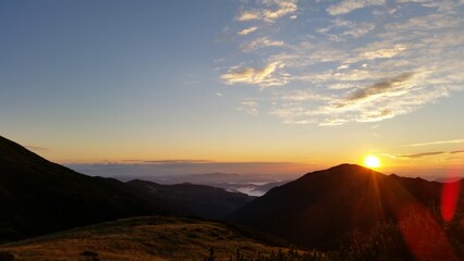 The sun sets slowly behind the mountain range, casting a warm orange glow across the landscape..