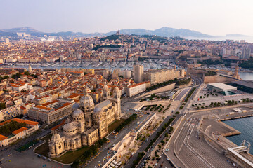 Fototapeta premium Scenic drone view of Marseille cityscape on Mediterranean coast overlooking Romanesque Cathedral of Saint Mary Major, medieval Fort Saint-Jean and Old Port with moored yachts, France