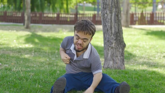 Dwarf young man having nervous breakdown slaps himself outdoors.