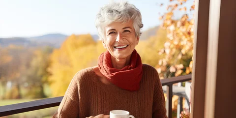 Schilderijen op glas Portrait of happy senior woman smiling drinking hot coffee or tea standing outdoor on the home balcony © britaseifert
