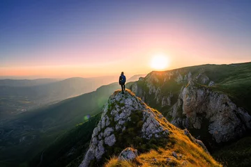Poster A man who hikers enjoys a break look at the top of the mountain at sunset adventure travel. © Malik Nalik