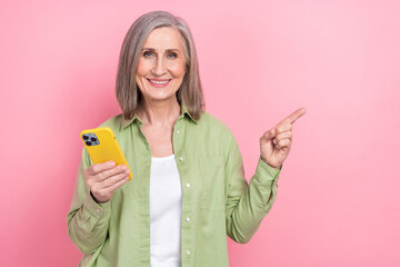 Photo of woman gray hair pensioner hold new gadget iphone indicating empty space finger true information isolated on pink color background