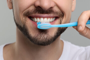 Man brushing his teeth with plastic toothbrush on light grey background, closeup