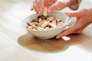 Brazil nuts in the diet. Healthy fats in the diet. Brazil nuts in a white ceramic cup in hand on a wooden table.hand takes brazil nuts from a plate close-up.Nuts and seeds.Useful healthy snack. 