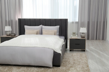 Stylish bedroom in soft light colors with comfortable bed and bedside tables. Interior design